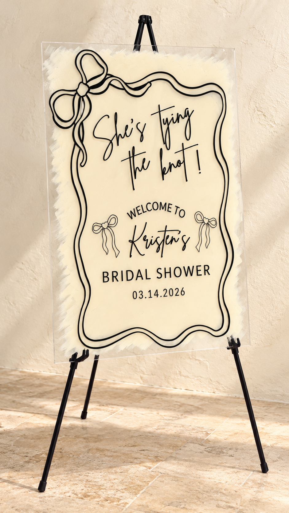 She’s tying the knot acrylic welcome sign styled against a warm ivory wall