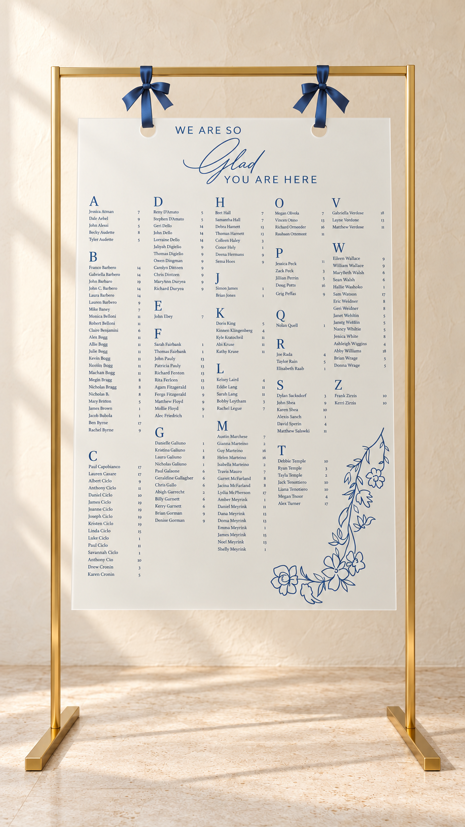 Frosted acrylic seating chart hanging from blue ribbons on a gold metal stand